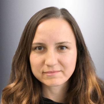 A woman with long, wavy brown hair and a neutral expression poses against a gradient gray background. The image conveys a professional or formal tone.