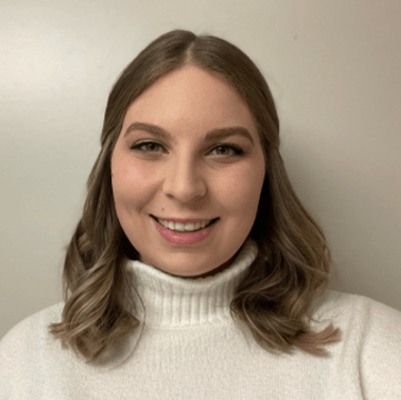 Smiling woman with shoulder-length hair, wearing a white turtleneck sweater. The simple background emphasizes her friendly expression.